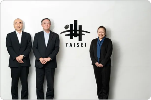 大成建設株式会社のオフィスで、3名の社員が並んで立っている様子（猪狩卓哉氏、宮地吾郎氏、鎌田美香氏）