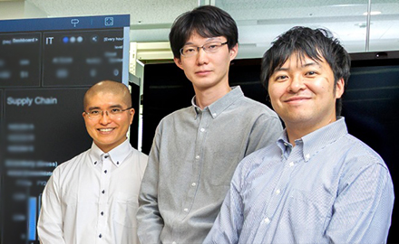 経営ダッシュボードの前に並んで立つNEC データ＆アナリティクス統括部 第三データアナリティクスグループ プロフェッショナル 山田 哲寛とNEC データドリブンDX統括部データアナリティクスサービシズ・デリバリーグループ担当 亀谷 純、そしてNECデータドリブンDX統括部 BI・事業開発グループ主任 増本 健