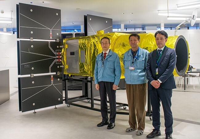 人工衛星模型の前に並ぶNECスペーステクノロジーの檜原氏、松原氏とNECの原田氏